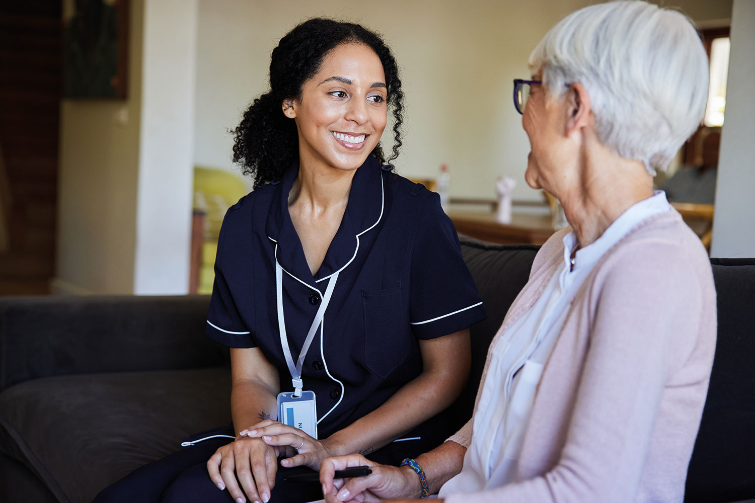photo of smiling uniformed carer chatting with older woman in her front room