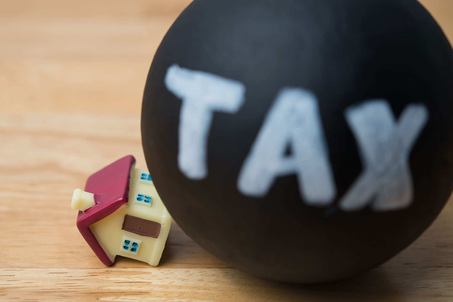 photo of big black bowling bowl with ‘tax’ written on the side rolling over a small 3D red roofed toy house