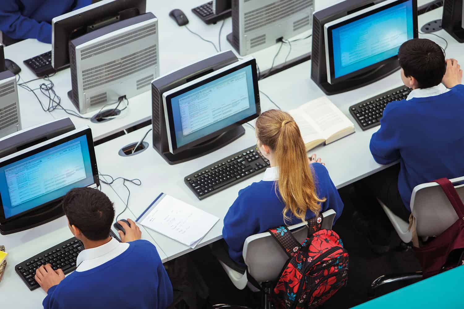 photo, from above and behind, of three secondary-age pupils in schools uniform sitting in front of computer screens and keyboards