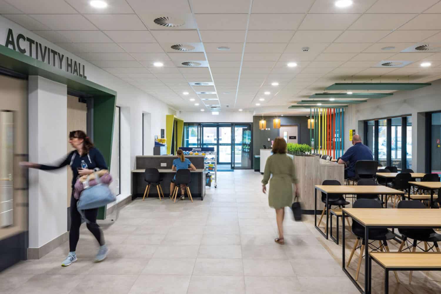 photo of reception area of Warsop Health Hub, with a woman in gym gear going through a door on the left and another woman with her back to us walking away from a seating area to the right