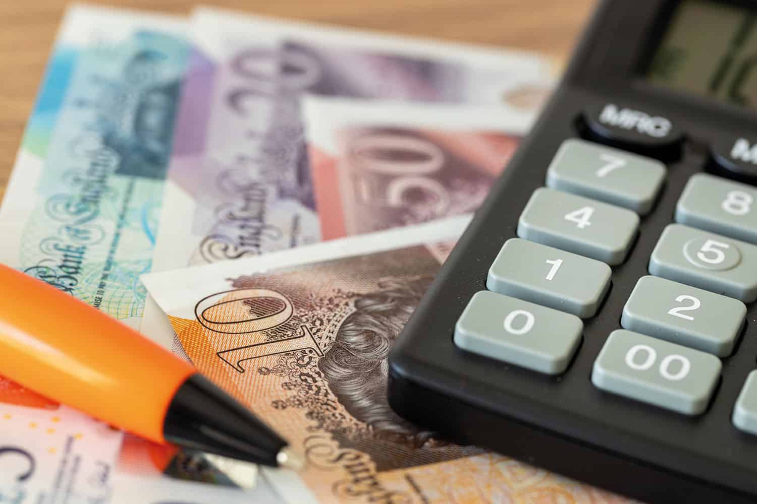 montage close-up of UK sterling notes, a calculator and a ballpoint pen