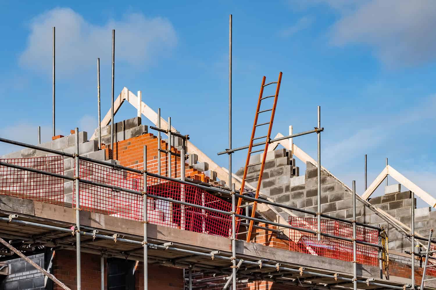 photo of the partially built roof of a new house surrounded by scaffolding set against a blue sky