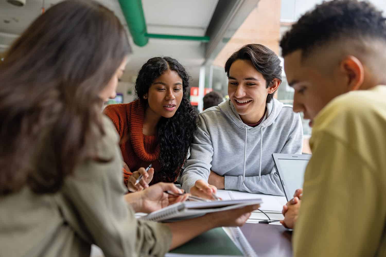 photo of three young people studying together, smiling and looking at exercise books